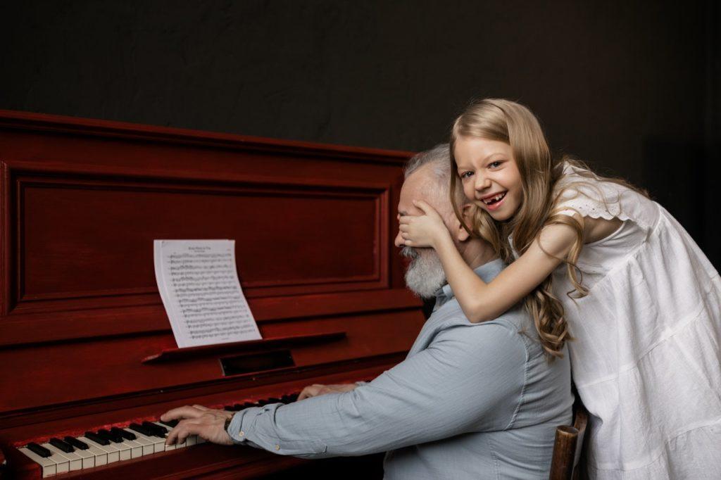 Mann, der Klavier spielt, während seine Enkelin ihm die Augen zuhält.
