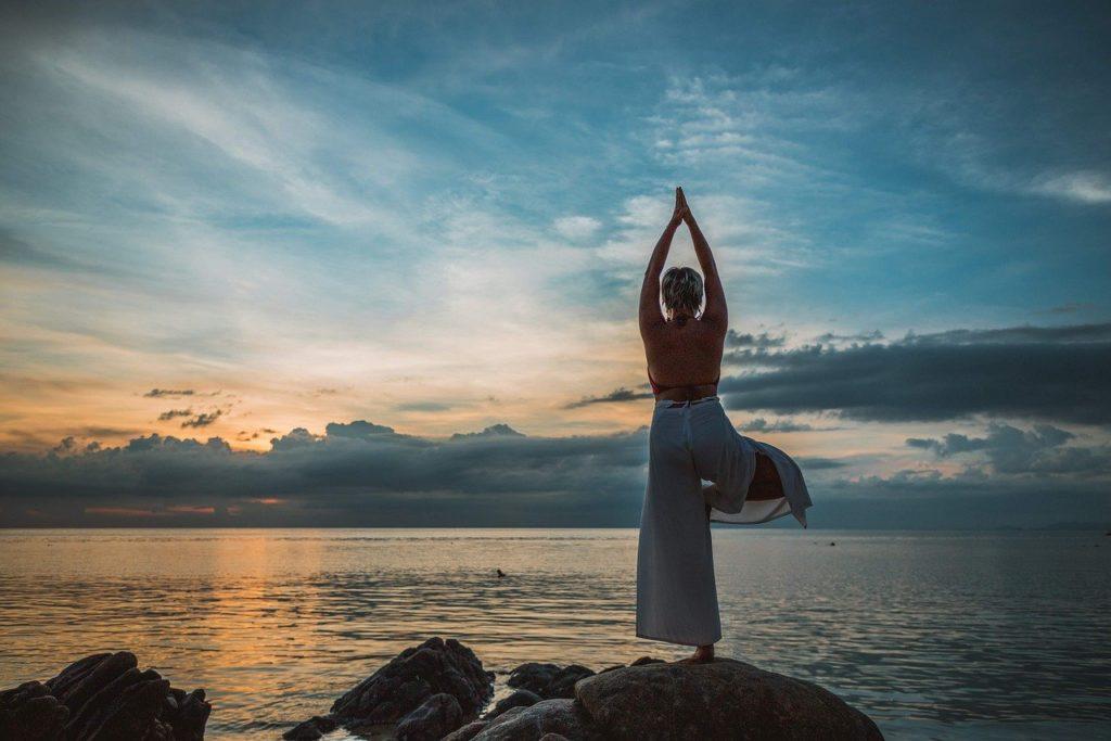 Frau beim Yoga am Strand während eines Sonnenuntergangs