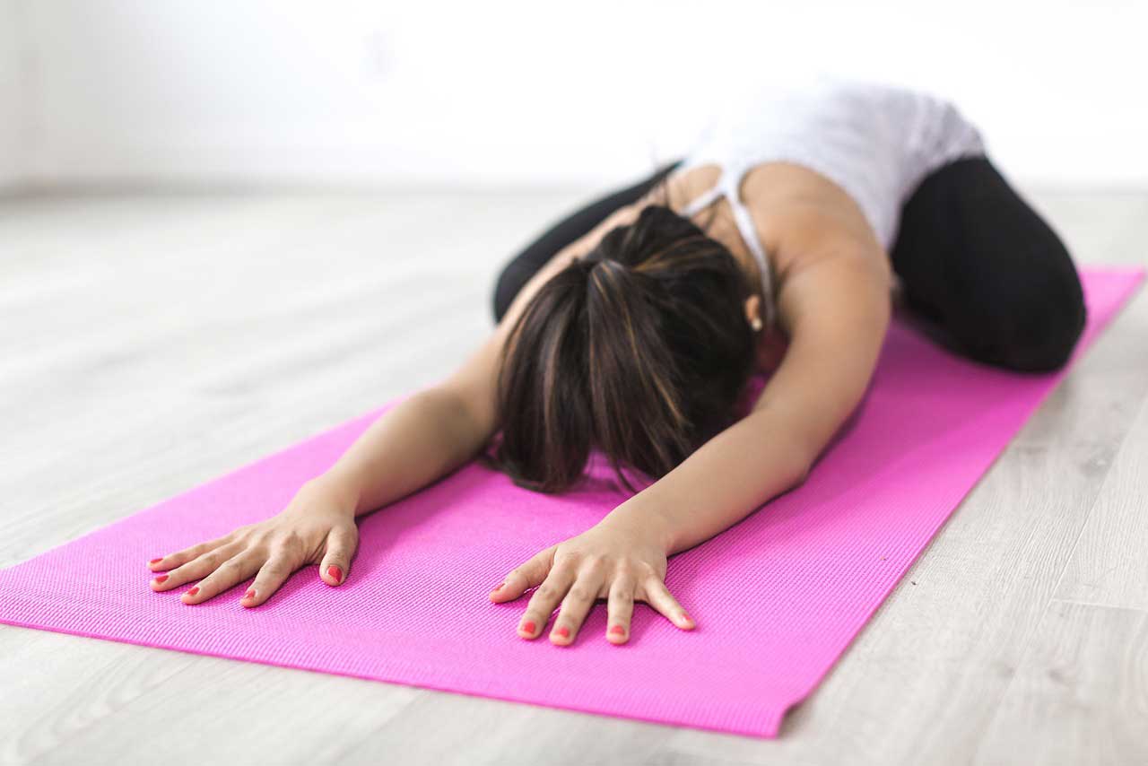 Eine Frau liegt in Yoga Kindpose auf einer pinken Yogamatte